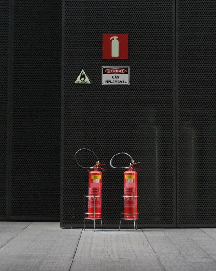 Dois extintores em suportes de piso, com placas de sinalização na parede